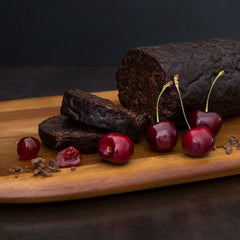 Two packages of Double Choc Cherry Pudding one log wrapped in calico with ribbon and the other in a vacuum sealed bag from Adamstown Pudding Kitchen on a white background.
