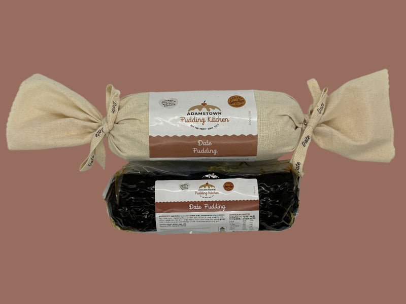 Two packages of Date log Pudding from one calico wrapped with ribbon and the other in a vacuum sealed bag Adamstown Kitchen on a white background