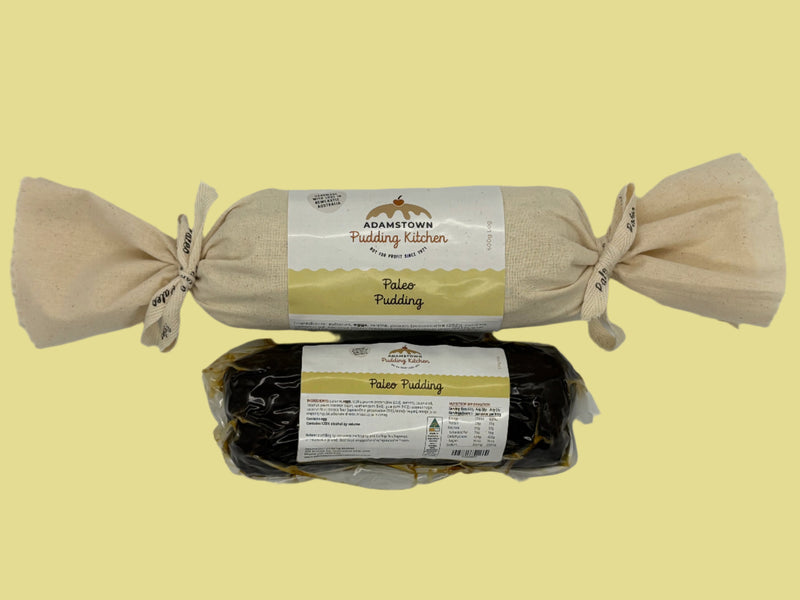 Two packages of Adamstown Pudding Kitchen Paleo Pudding one wrapped in calico with ribbon and one in a vacuum sealed bag on a white background